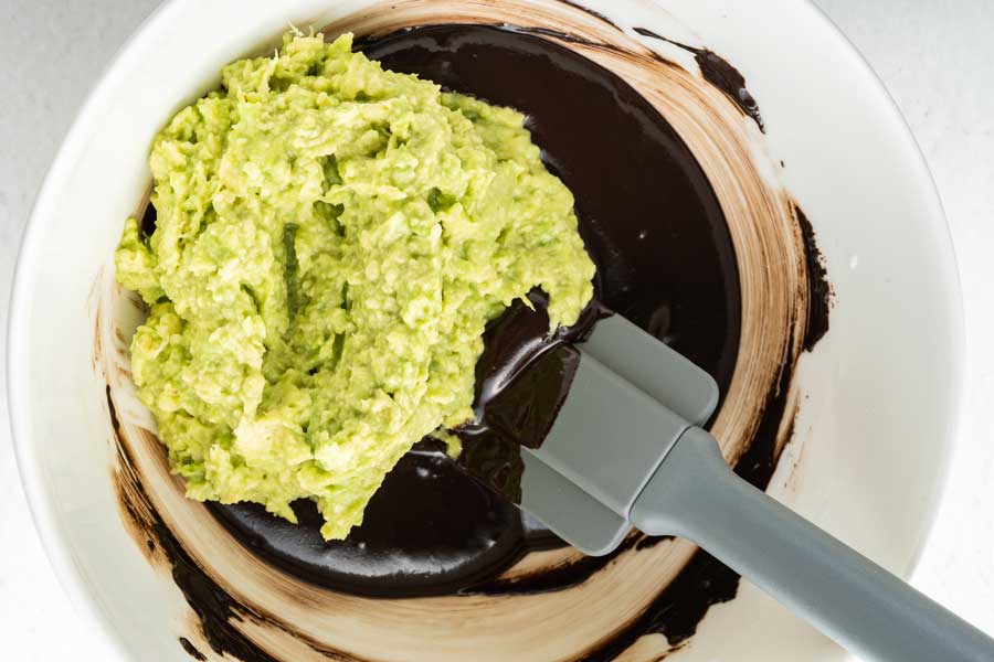 The picture shows the mixing of mashed avocado with melted chocolate in a white bowl.