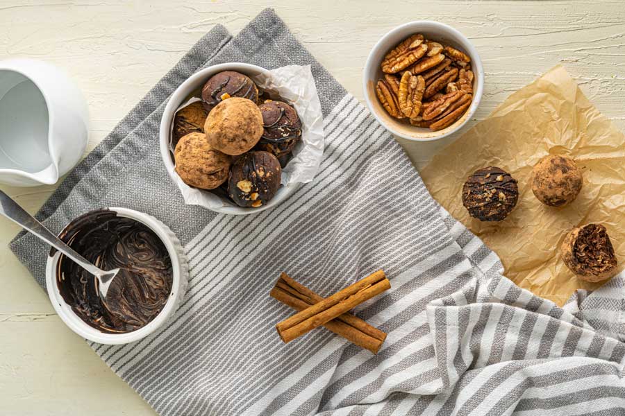 Chocolate truffles rolled and coated in a bowl with some of the coatings like pecans and melted chocolate in separate bowls on the side.