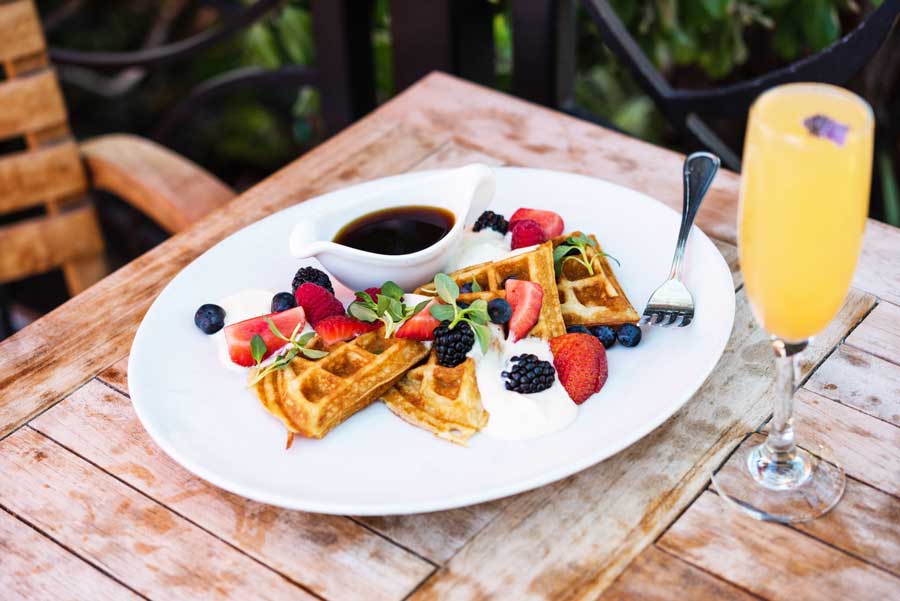 waffle with fruit with a mimosa on a wooden table