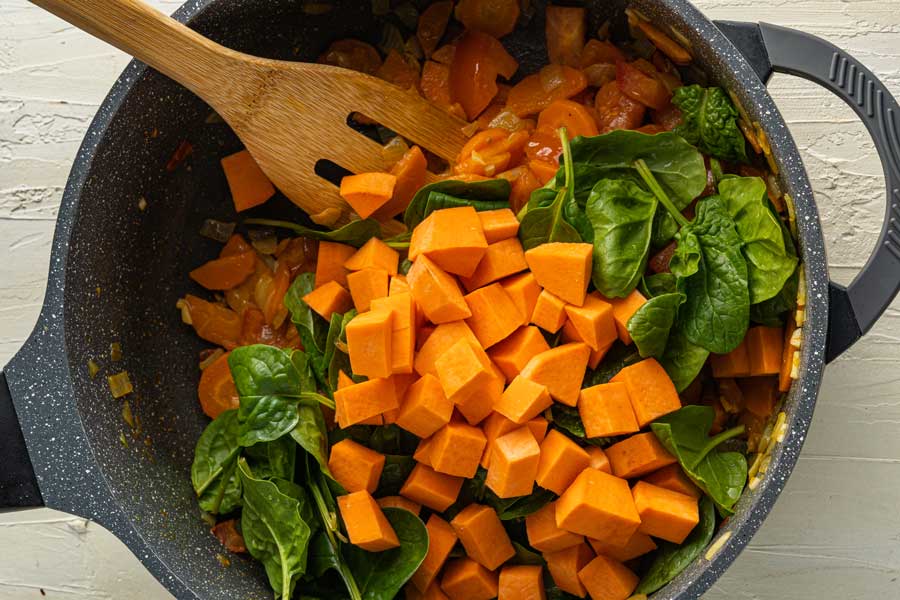 Adding sweet potatoes and spinach to the pot while making the sweet potato lentil soup.