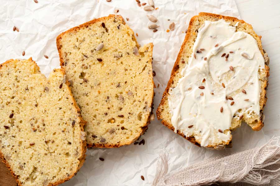 Slices of the seed bread spread out on a surface ready to eat with cream cheese spread on one of them.