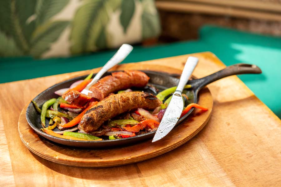two sausages on a cast iron plate with peppers and onions