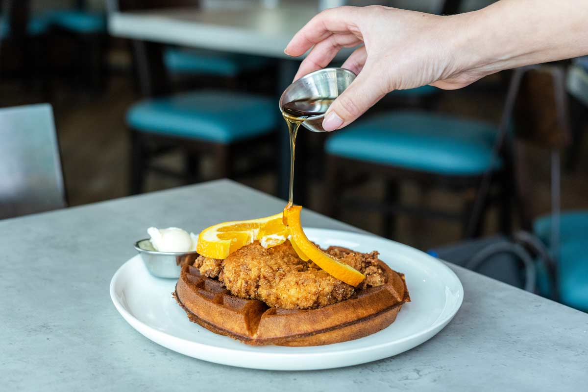 syrup being poured over fried chicken and waffles