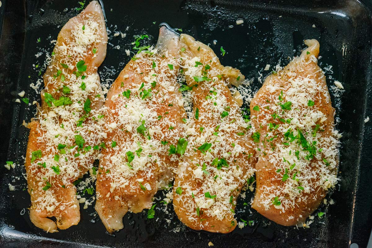 raw chicken breasts sprinkled with garlic and parmesan cheese in baking pan