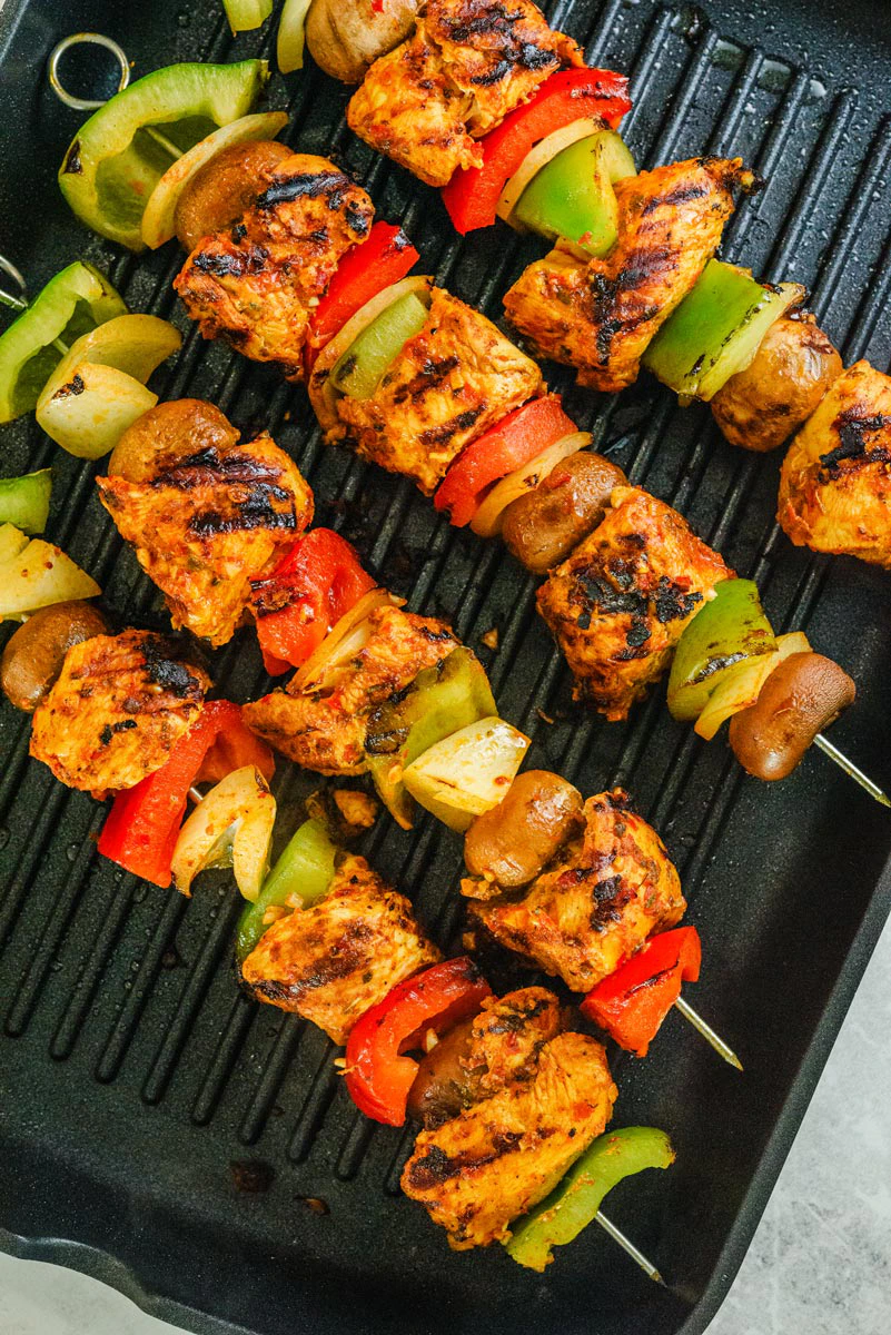 Grilled chicken kabobs with red peppers and green onions on a black grill pan with char marks.